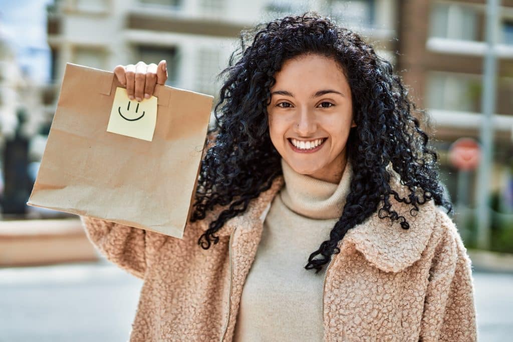 jeune femme hispanique souriante confiante tenant sac papier emporter dans rue
