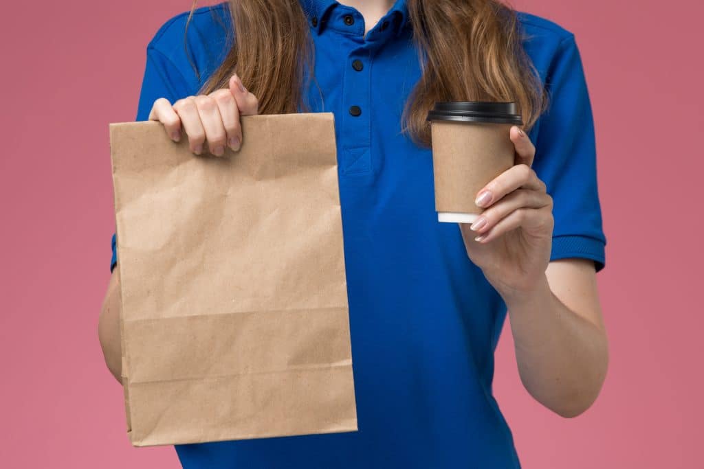 vue rapprochee avant courrier feminin uniforme bleu tenant tasse cafe brun paquet nourriture uniforme travail service bureau rose clair entreprise livraison